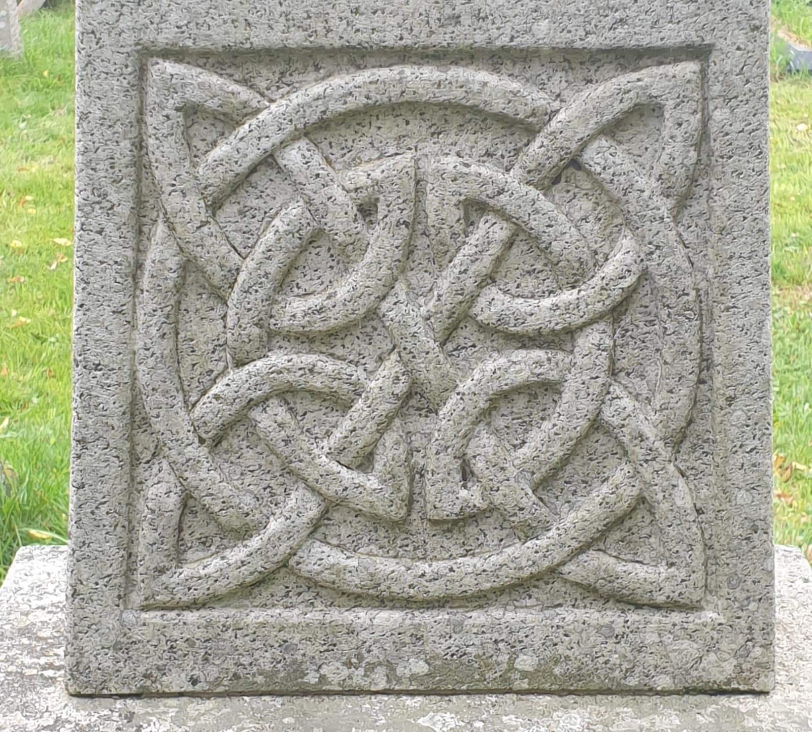 A carved Celtic knot on a gravestone in St James churchyard, set against the grass