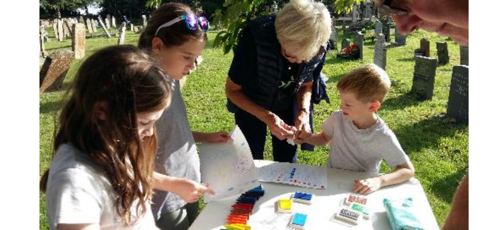Children and an adult making crafts at a table in the churchyard during Muddy Church