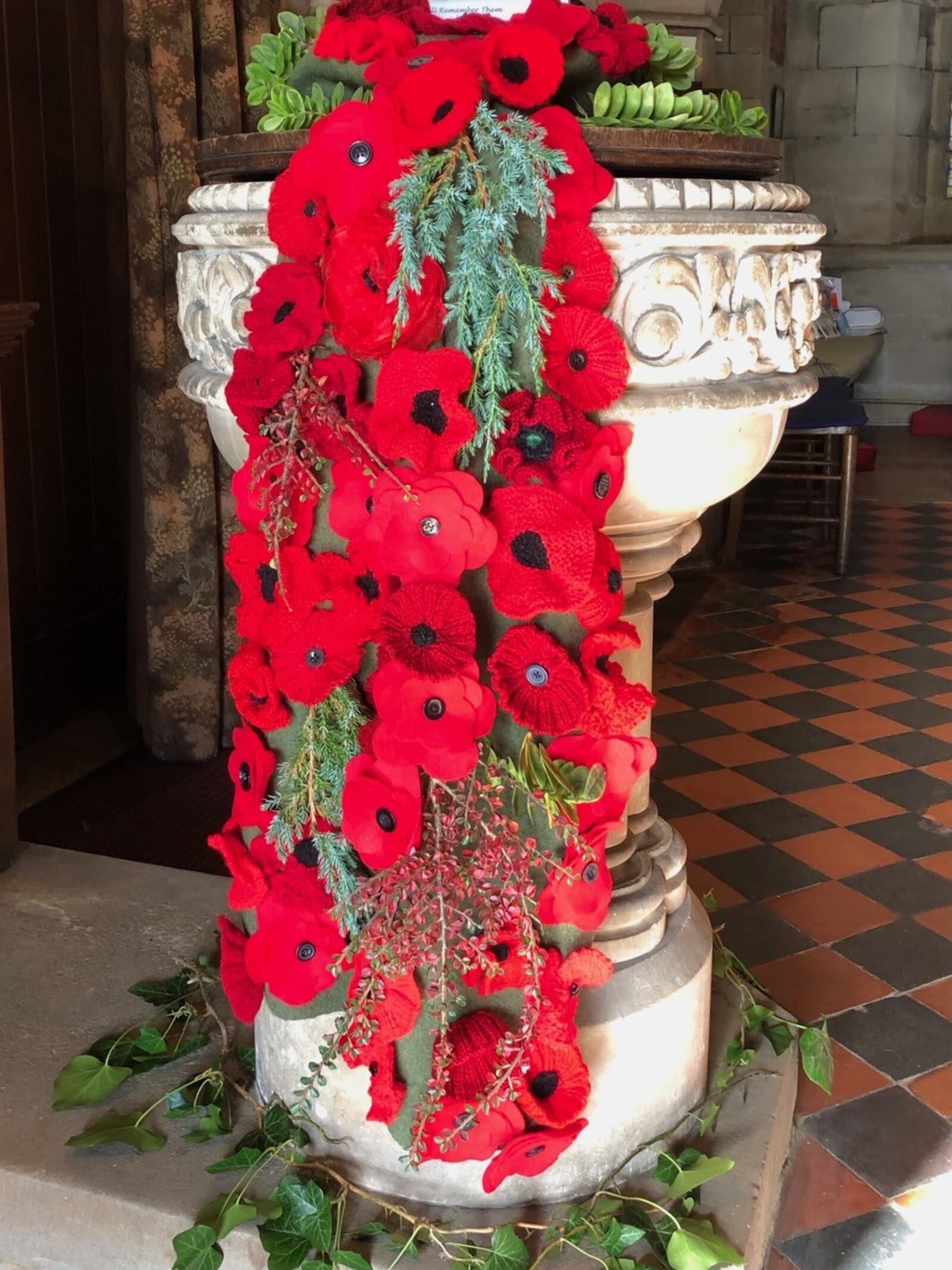 A cascade of knitted poppies dressing the font inside St James for Remembrance